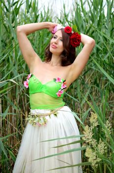 Female model from Poland posing near the lake, surrounded by reeds. Woman wearing flowers' wreath, colorful dress. Chestnut hair color.