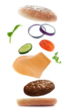 Burger ingredients falling into place to create a sandwich over a white background 