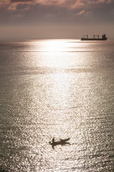 Paddle boat and cargo ship. The sun was reflecting off the sea in the evening.