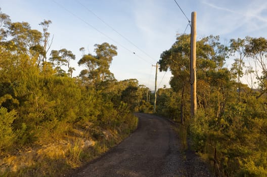 Photograph of an Australian dirt road with electric poles in the sunset