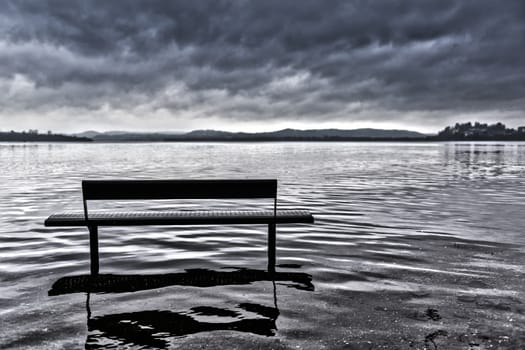 bench on Lake Varese overflows in autumn season with cloudy sky, Lombardy - Italy