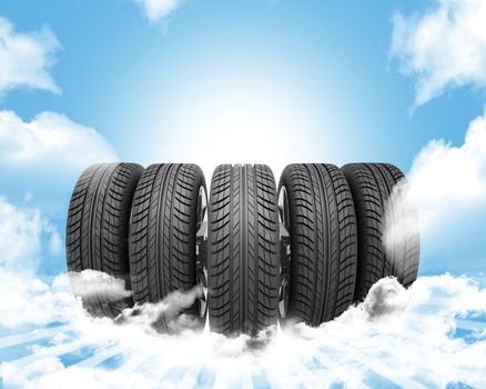 Wedge of new car wheels. Blue background is sky with clouds and stripes at bottom