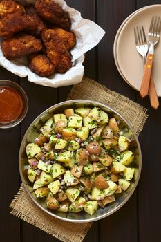 Salad of jacket potato, red onion and herbs with homemade breaded and fried chicken wings, photographed overhead on dark wood with natural light