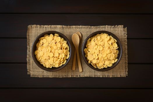 Crispy corn flakes breakfast cereal in rustic bowls with small wooden spoons, photographed overhead on dark wood with natural light