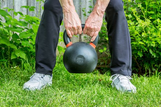 fitness workout with a heavy iron competition kettlebell (62lb/28 kg) on green grass in backyard - outdoor fitness concept