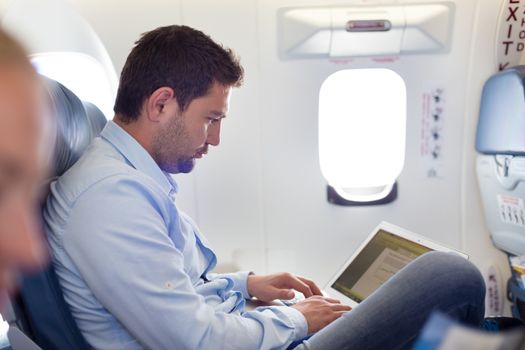 Casually dressed middle aged man working on laptop in aircraft cabin during his business travel. Shallow depth of field photo with focus on businessman eye.