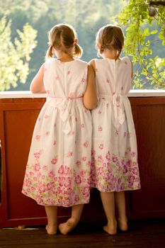 Twin girls in summer dresses on porch looking at the view