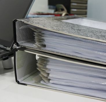 Two black folders. There are many papers put inside, placed on a desk at the office.                               