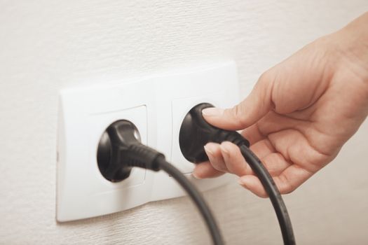 Woman pluging cable to the electric outlet