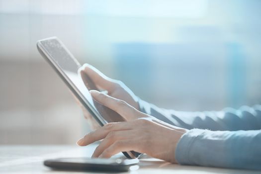 Hands of woman working with digital tablet behind the glass at office