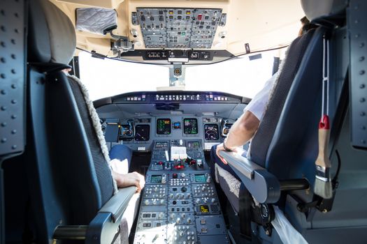 Rear view of pilot and copilot flying comercial airplane. Interior of airplane cockpit. Instrument panels in pilot's cabin.