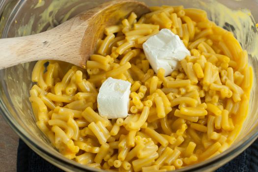 Macaroni and cheese in a bowl with cream cheese chucks and a wooden spoon.