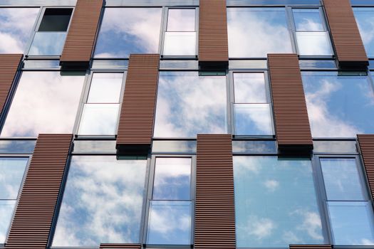 Blue overcast sky and clouds reflected in mirror windows of new modern office building with one open section