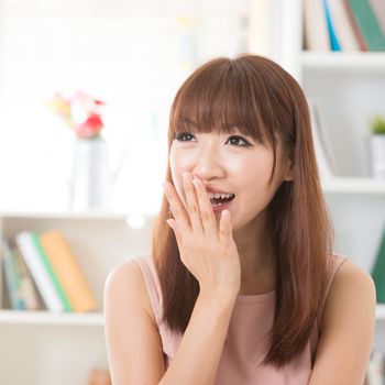 Portrait of happy Asian girl laughing and hand covering mouth looking away. Young woman indoors living lifestyle at home.