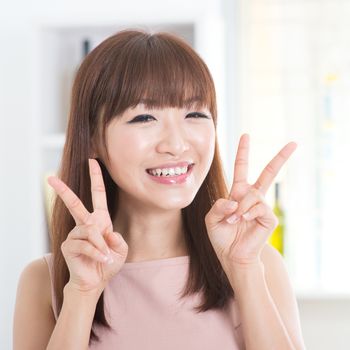 Portrait of attractive Asian girl showing peace or v hand sign. Young woman indoors living lifestyle at home.