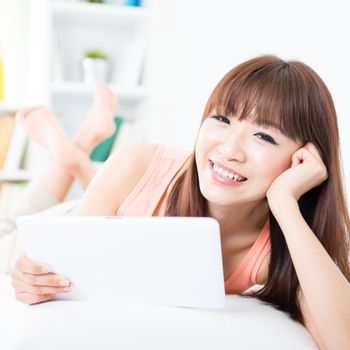 Portrait of attractive Asian girl smiling and using touch screen tablet on bed. Young woman indoors living lifestyle at home.