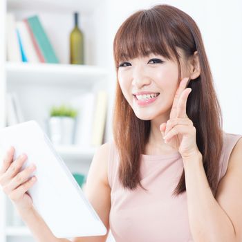 Portrait of attractive Asian girl using digital tablet and showing v hand sign. Young woman indoors living lifestyle at home.