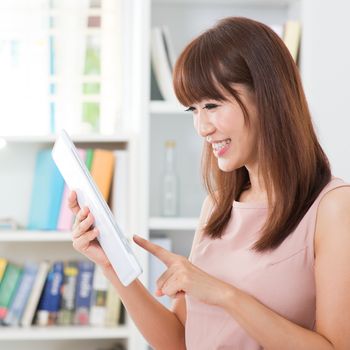 Portrait of attractive Asian girl laughing while using social media on tablet. Young woman indoors living lifestyle at home.