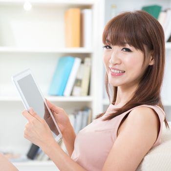 Portrait of attractive Asian girl using digital pc tablet and smiling happily looking at camera. Young woman indoors living lifestyle at home.