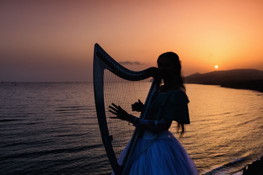 Silhouette woman plays harp by the sea at sunset in Santorini, Greece