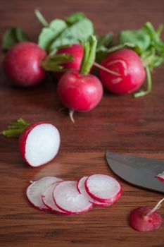 Fresh radishes sliced on a wooden cutting board with a knife.