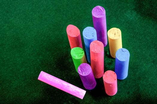 Broken pieces of chalk, all of different lengths and colours stand upright on a green surface. One piece lies on it's side.