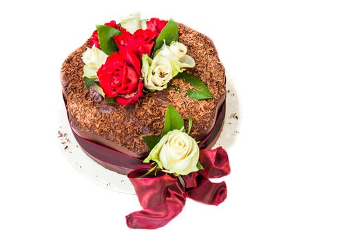 Chocolate cake with red and white roses and a red bow viewed from a high angle on a white background.