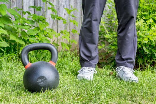 fitness workout with a heavy iron competition kettlebell (62lb/28 kg) on green grass in backyard - outdoor training concept