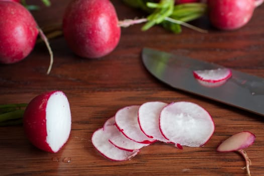 Fresh radishes sliced on a wooden cutting board with a knife.