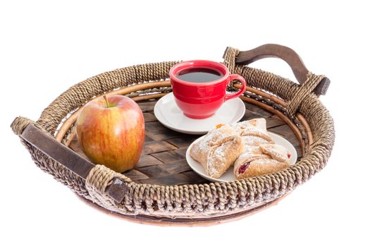 Fresh apple, crossover pastries filled with cheese, strawberry and peach and a cup of espresso coffee served on a rustic wicker tray for breakfast, isolated on white low angle
