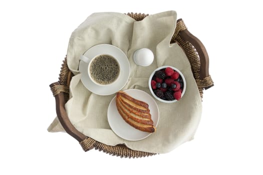 Tasty breakfast for one on a rustic wicker tray with a cup of fresh espresso coffee, boiled egg, ramekin of fresh assorted berries and a crispy pastry viewed from above isolated on white