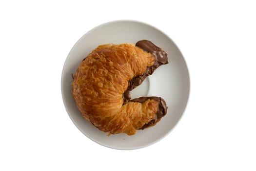 Freshly baked flaky buttery croissant filled to overflowing with hazelnut chocolate spread oozing onto the plate, tempting breakfast viewed from overhead isolated on white