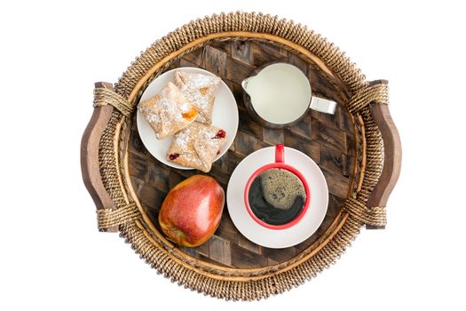 Fresh fruit and pastries for breakfast with a ripe red organic apple, crossover pastries with cheese, peach and strawberry filling and a cup of black coffee with a jug of milk, isolated overhead view