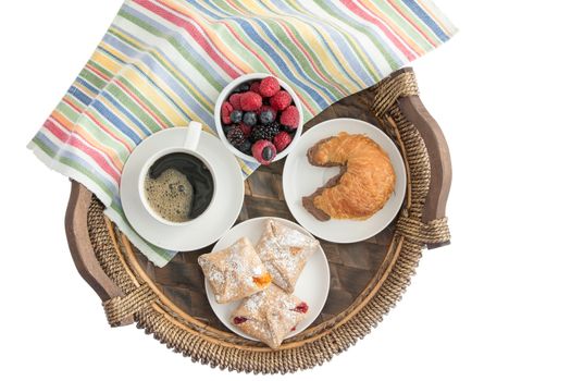 Tasty morning breakfast on a wicker tray with freshly baked pastries filled with cheese, strawberry and peach, a croissant with chocolate hazelnut spread, coffee and fresh berries, overhead on white