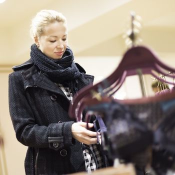 Woman shopping lingerie . Shopper looking and choosing clothing indoors in store. Beautiful blonde caucasian female model wearing winter coat and fashionable knitted cap.