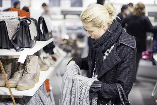 Woman shopping clothes. Shopper looking at clothing indoors in store. Beautiful blonde caucasian female model. 