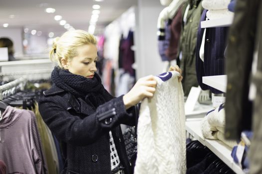 Woman shopping clothes. Shopper looking at clothing indoors in store. Beautiful blonde caucasian female model. 