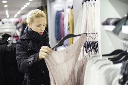 Woman shopping clothes. Shopper looking at clothing indoors in store. Beautiful blonde caucasian female model. 