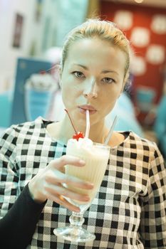 Blond caucasian woman drinking milkshake with straw in american diner.