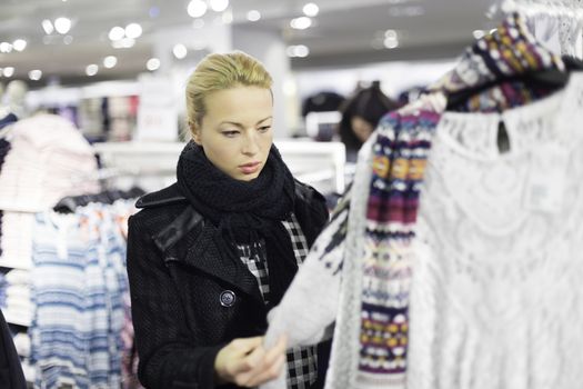 Woman shopping clothes. Shopper looking at clothing indoors in store. Beautiful blonde caucasian female model. 
