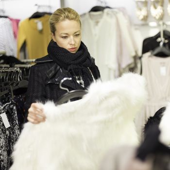 Woman shopping clothes. Shopper looking at clothing indoors in store. Beautiful blonde caucasian female model. 