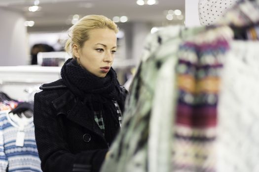 Woman shopping clothes. Shopper looking at clothing indoors in store. Beautiful blonde caucasian female model. 