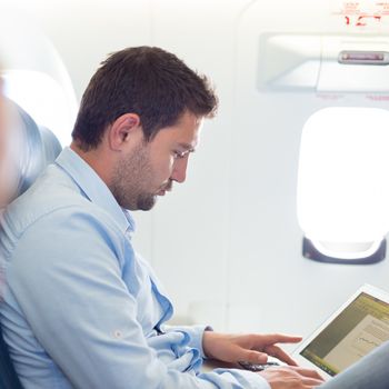 Casually dressed middle aged man working on laptop in aircraft cabin during his business travel. Shallow depth of field photo with focus on businessman eye.