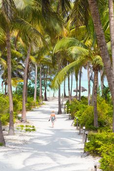 Relaxed  woman on vacations wearing sarong, walking barefooted trough lush green palm garden of  holiday resort on Paje beach, Zanzibar, Tanzania. Vertical composition. Copy space.