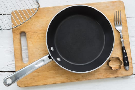 Top view of kitchenware, empty black pan, fork, cookie cutter and plank putting on white wooden table, cooking or baking vintage style image.