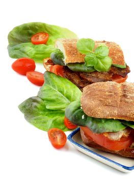 Ciabatta Sandwiches with Bacon, Tomato, Lettuce, Sauces and Basil closeup on white background