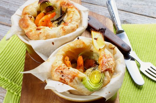 Two Ramekins with Puff Pastry Snacks with Shrimps, Leek and Cheese Oven-Baked on Wooden Cutting Board with Fork and Knife