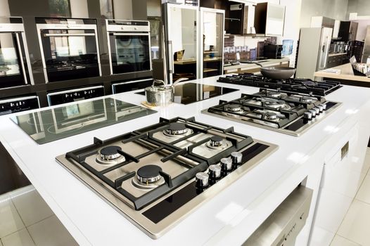 Rows of brand new gas stoves and ovens with stainless steel trays in appliance retail store