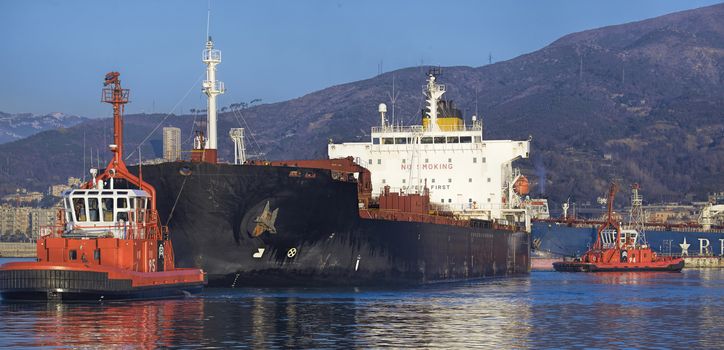 tugs at working near a ship in Genoa oil harbor, Italy