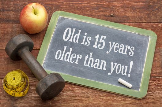 Old is 15 years older than you  -  slate blackboard sign against weathered red painted barn wood with a dumbbell, apple and tape measure